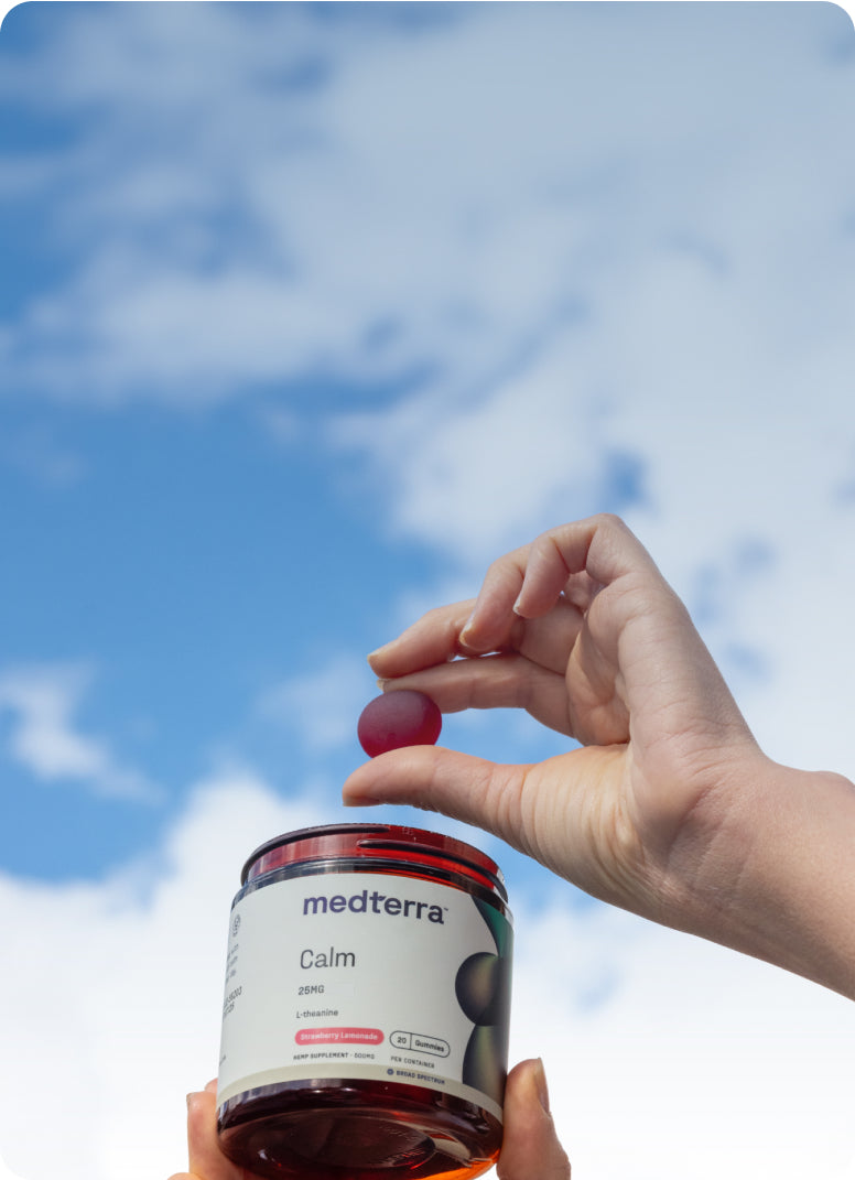 Hand holding red gummy over jar labeled medterra Calm 25MG L-theanine Strawberry Lemonade 20 Gummies HEMP SUPPLEMENT 500MG
