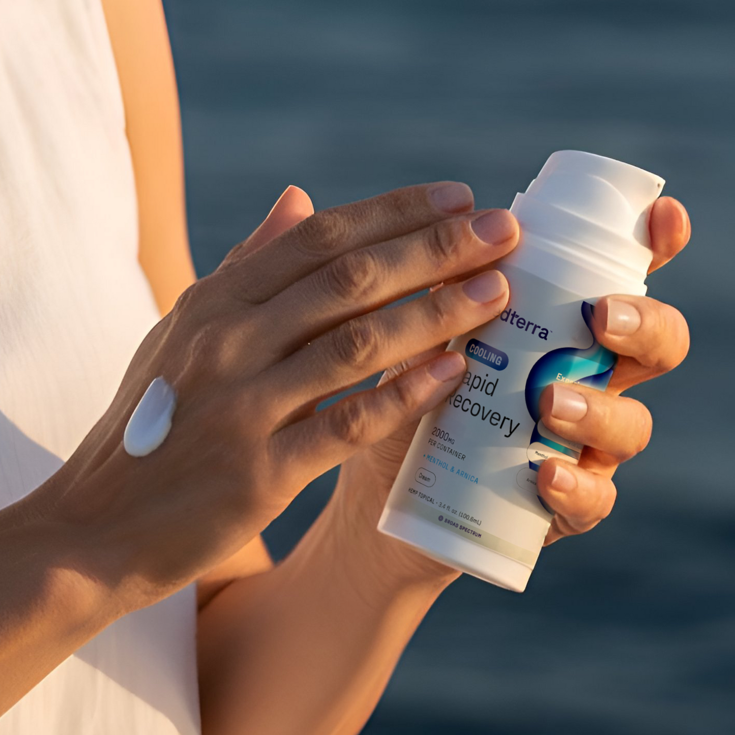 Hands applying cream from doterra bottle labeled "COOLING Rapid Recovery 2000mg per container Menthol & Arnica"