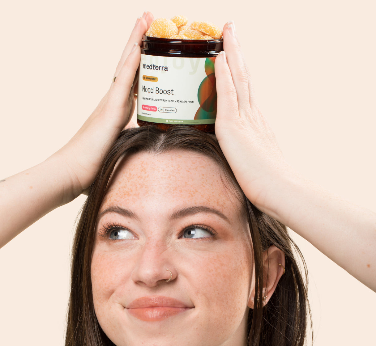 Young woman balancing a jar labeled 'medterra Mood Boost Strawberry Citrus 20 Gummies Full Spectrum Hemp' on her head